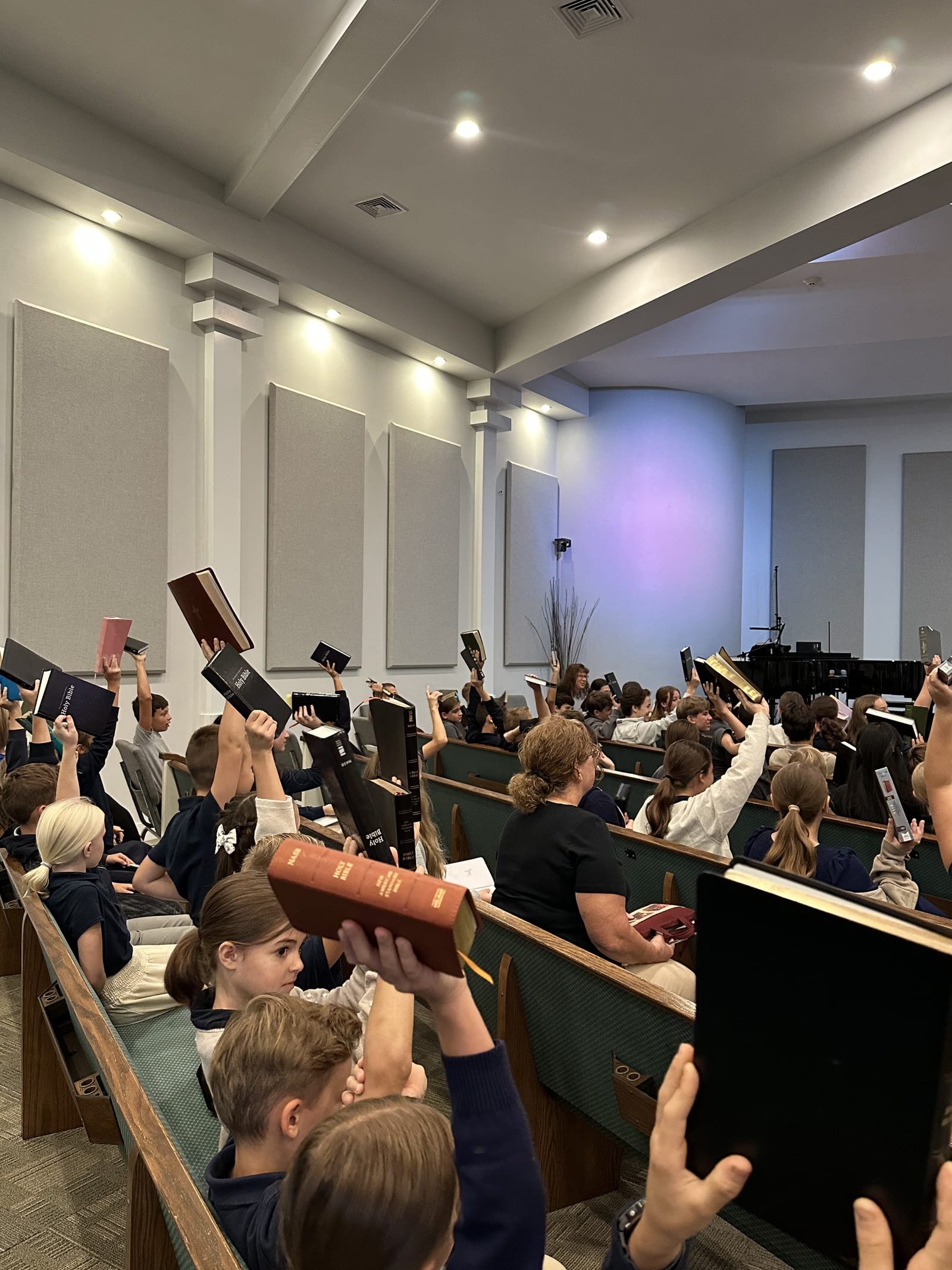 Students and families raising Bibles during chapel at Gospel Light Academy